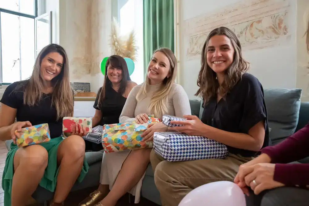 A group of friends laughing while wrapping gifts at a long table